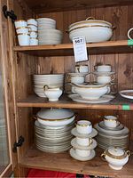 Three shelves filled with pieces of white Limoges china featuring gold trim, including stacked plates, cups with saucers, and various serving dishes.