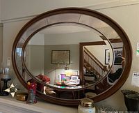 Front view of the oval wall mirror showing the wood frame, beveled edges, and mottled outer rim mirror sections.