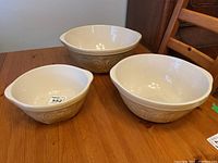 Three nesting ceramic bowls on wooden table, cream/beige with geometric pattern