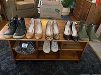 Full view of all shoes on a wooden table including pumps, boots, sneakers, and slides.