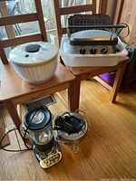 Full view of all items in the lot arranged on wooden chairs and floor, showing KitchenAid blender, Cuisinart fondue set, griddler, and Oxo salad spinner.