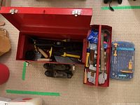 Red metal toolbox open showing tools including hammer, hand planes, gloves, and screwdriver sets