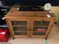 Front view of hardwood TV cabinet with two glass doors and two internal shelves, surface shows some wear.