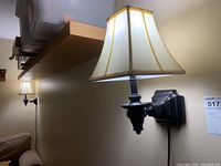 Two matching wall sconces mounted on a beige wall, illuminated to show fabric shades and black metal mounts.