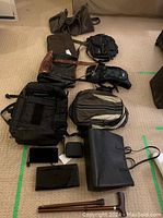 Full lot overview showing all bags on floor, including backpacks, messenger bags, wallets, and travel cane.