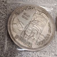 Reverse side of 1958 Canadian silver dollar coin showing British Columbia Centennial totem pole design with inscriptions and dates.