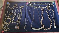 Multiple pieces of costume jewelry displayed on a blue velvet surface, including gold-tone and silver-tone necklaces, bracelets, chains, and a colorful crystal pendant.