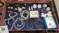 Overhead photo showing the full assortment of costume jewelry laid out inside a box including bracelets, earrings, necklaces, and pins on a blue felt base.