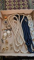Box of assorted costume jewelry including pearl necklaces, various earrings, and a brooch.