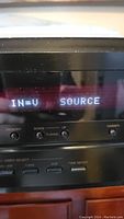 Close-up of the digital display panel of the Denon receiver showing input source information and physical buttons for tuning and selection.