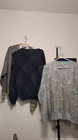 Four men's medium sweaters hanging on hangers showing patterns and colors