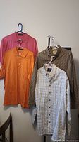 Four men's large tops hanging: includes two dress shirts and two polo shirts.