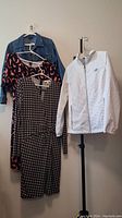 Four women's clothing items hanging on a stand: denim jacket, animal print dress, houndstooth dress, white zip-up hoodie