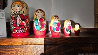 Front view of six wooden Russian nesting dolls lined up by size on a wooden surface, showing detailed hand-painted floral decoration.