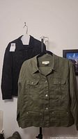 Photo of olive green cargo-style jacket and black floral embroidered knit jacket hanging on hangers