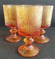 Four amber glass textured goblets shown from the front on black background.