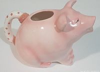 Photo showing the front and left side of the pink pig-shaped ceramic pitcher with polka dot handle and open top.