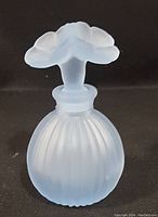 Front view of vintage frosted satin glass perfume bottle showing rounded ribbed body and floral stopper.
