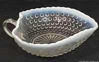 Vintage 1940s moonstone opalescent Fenton glass bowl with hobnail pattern, clear finger handle, scalloped white rim, sunburst pattern on base, shown from top angle on black background.