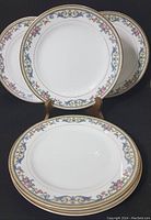Five Noritake salad plates displayed with floral scroll and gold trim border