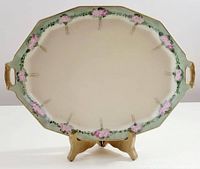Front view of the oval serving platter showing hand painted pink and green floral border on cream background with gold accents and handles.