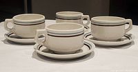 Four white granite vitrified cups and saucers arranged showing front and side views, highlighting their shape, handle design, and rim bands.