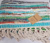 Close-up photo displaying multicolored hand woven cotton rug with fringe and Rivancio tag.