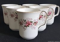 Six Royal Albert coffee mugs arranged in a group, showing the floral rose pattern and gold-trimmed rims and handles.