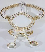 Photo of five hand painted Nippon porcelain pieces displayed with stands, showing intricate gold and pink floral designs on white porcelain.