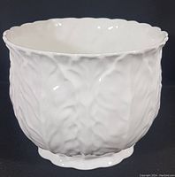 Full view of the white porcelain jardiniere showing the textured leaf relief pattern and scalloped rim.