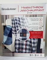 Front view of the boxed Brookstone Heated Throw showing packaging details including 4 heat settings, ultra-soft fabric, automatic 4-hour auto-off, and one-touch remote control.