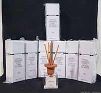 Seven sealed white boxes of Omnibus fragrance diffusers arranged in a row, one upright in the center showing wooden top sticks inserted.