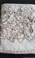 Close-up image showing ivory fabric with taupe lacey floral patterns and openwork design.