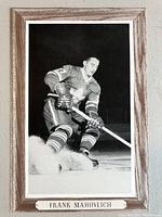 Front view of the framed black and white hockey photo of Frank Mahovlich in Toronto Maple Leafs uniform with woodgrain border and metal nameplate.