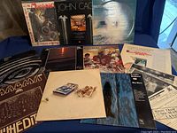 Photo of 12 vinyl record albums arranged showing covers with various art styles and titles including Stomu Yamashta and John Cage.