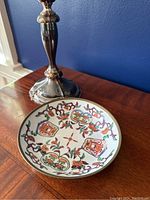 Photo showing the top and interior of the bowl with detailed floral and geometric painted patterns in multiple colors, placed on a wooden surface with a silver candlestick beside it.