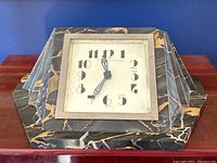 Front view of the clock showing the hexagonal black and gold marble case and white clock face with black art deco numerals and hands.