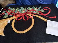 Full view of the holiday area rug displaying the black background with gold horn and red ribbon with green holly leaves design.