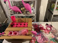 Photo showing flamingo lawn ornaments, plastic flamingo flamingo wine glasses in boxes and various flamingo party supplies including headbands and plates.
