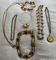 Lot of vintage jewelry on white background, showing a bracelet, multiple necklaces including a multi-colored stone necklace, leaf pendant, and chain designs