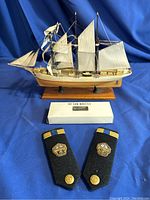 Front view of Gazela ship model with bosun's whistle box and naval shoulder insignias on blue cloth background