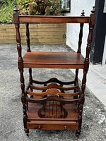 Full front view of vintage oak cabinet showing three shelves, spindle legs, carved wooden dividers for holding items, and wheels.