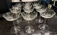 Thirteen vintage etched champagne coupe glasses arranged in rows, showing the set count and uniform style.