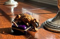 Side view of the vintage Russini crouching tiger trinket box on a wooden surface with sunlight highlighting details.