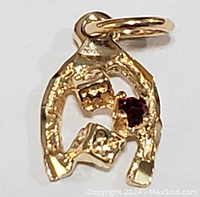 Close-up front view of the yellow gold horseshoe pendant with two dice and ruby distinctly visible.