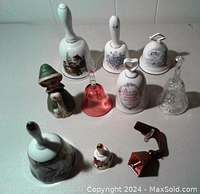 Full lot of 10 decorative bells arranged on a white surface, showing variety of materials and shapes.