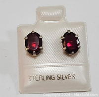Front view of the sterling silver garnet earrings showing oval red garnet stones set with six claws, displayed on a marked 'STERLING SILVER' white holder.