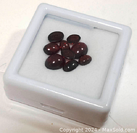 Nine polished oval cabochon garnet gemstones arranged in a white square display box on a white background.