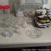 Photo showing a group of clear pinwheel crystal drinking glasses with faceted stems next to several clear dessert plates with star and lattice cut patterns.