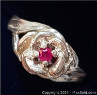 Close-up front view showing the raised floral design and ruby gemstone held by four claw prongs on the sterling silver ring.